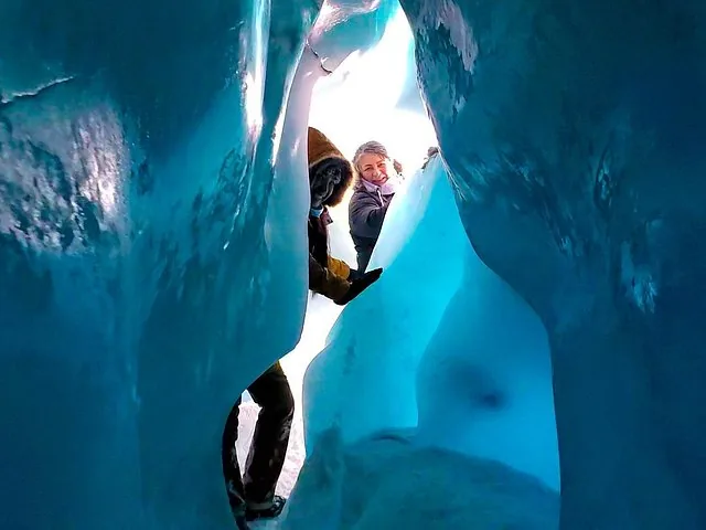Two people exploring a vibrant blue ice cave within a glacier.