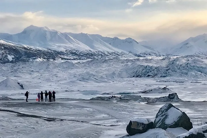 Eine Gruppe von Menschen steht auf einem weiten, schneebedeckten Gletscher.
