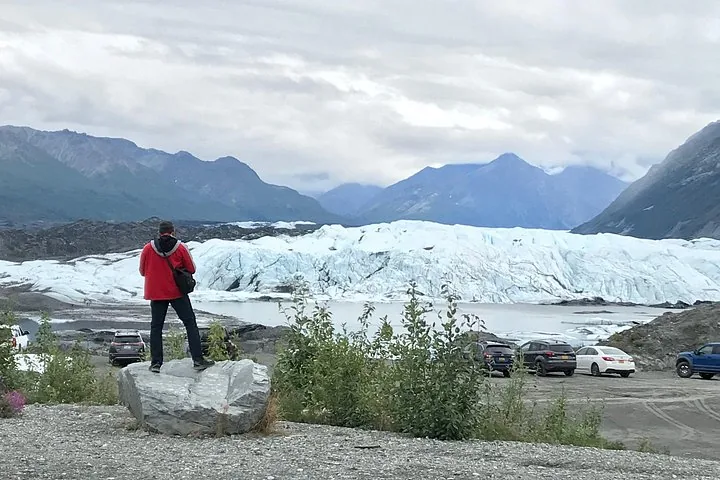 Person looking at a glacier from a parking area with cars.