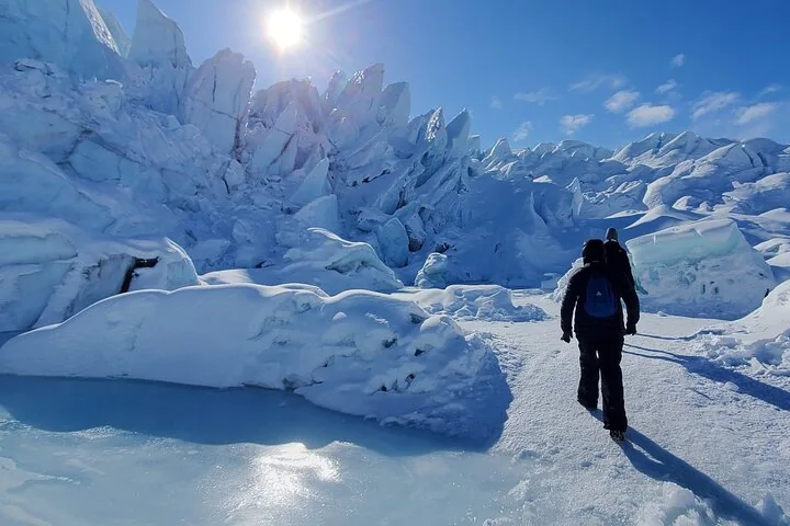 Wanderer laufen auf einem schneebedeckten Gletscherpfad auf zerklüftete Eisformationen zu.