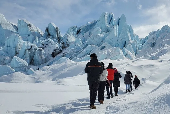 Eine Gruppe von Wanderern geht auf einem schneebedeckten Pfad durch große Gletscherformationen.