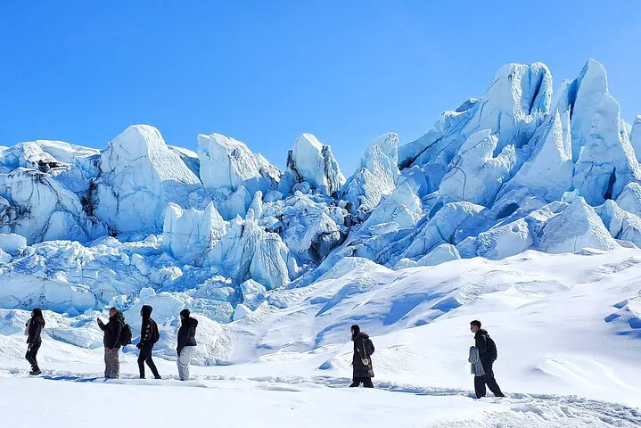 Eine Gruppe von Menschen geht im Gänsemarsch über einen riesigen Gletscher.